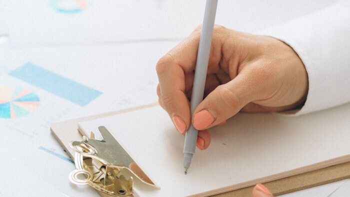 Detail of hands writing with a pen on a clipboard over financial papers.