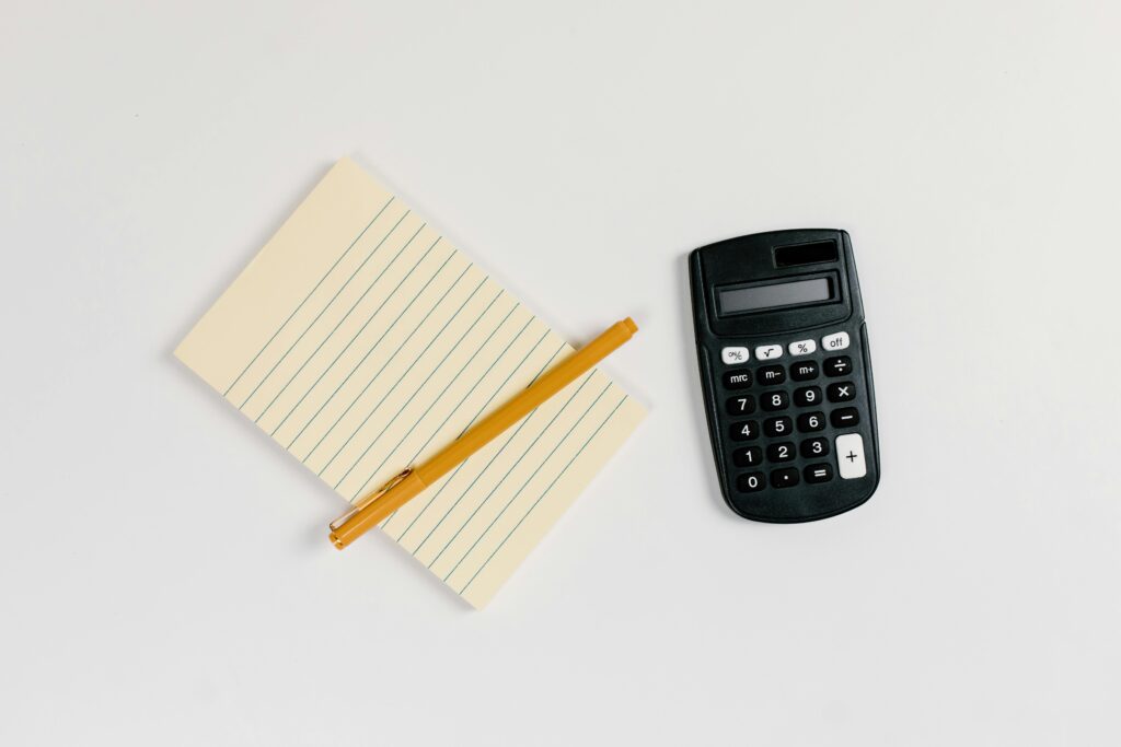 Minimalist flat lay of a calculator and lined notepad with a gold pen on a white surface.